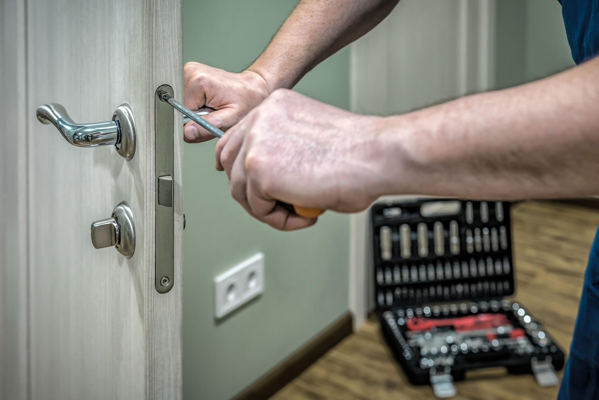 Professional locksmith worker installing, working with house door lock using screwdriver